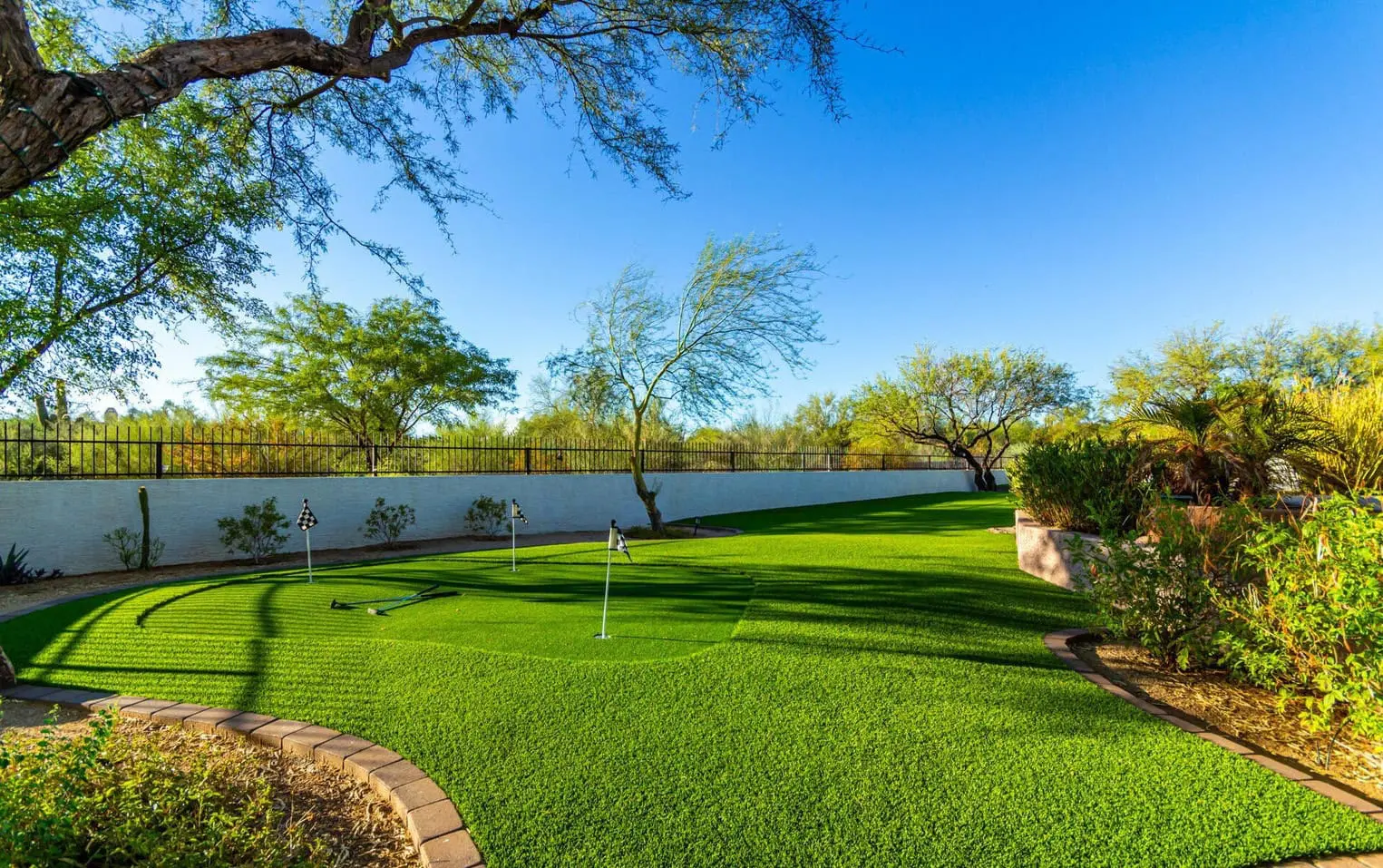 A lush, green backyard in Deer Valley features a mini-golf putting green surrounded by trees and shrubs. The sunny sky and the artificial grass create a serene and inviting outdoor space perfect for relaxation and recreation.